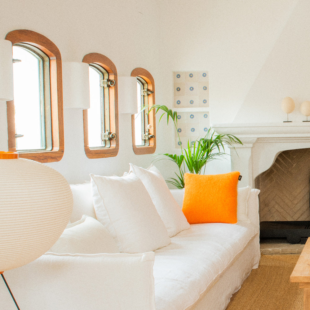 A living room with a white sofa and an orange mohair pillow on it.