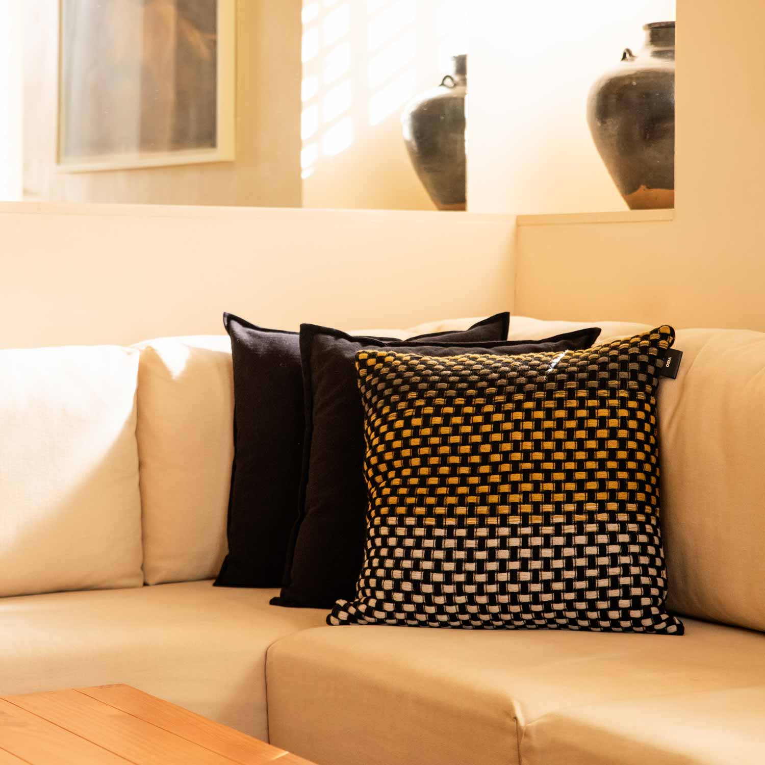 A basketweave wool pillow in a black, white and yellow gradient on a white sofa.