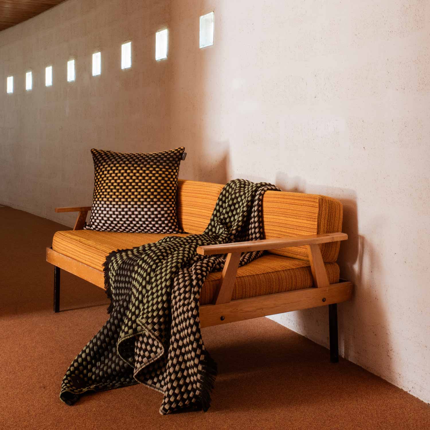 A basketweave wool blanket and pillow in a color gradient of black, yellow and white, on a sofa in a living room.