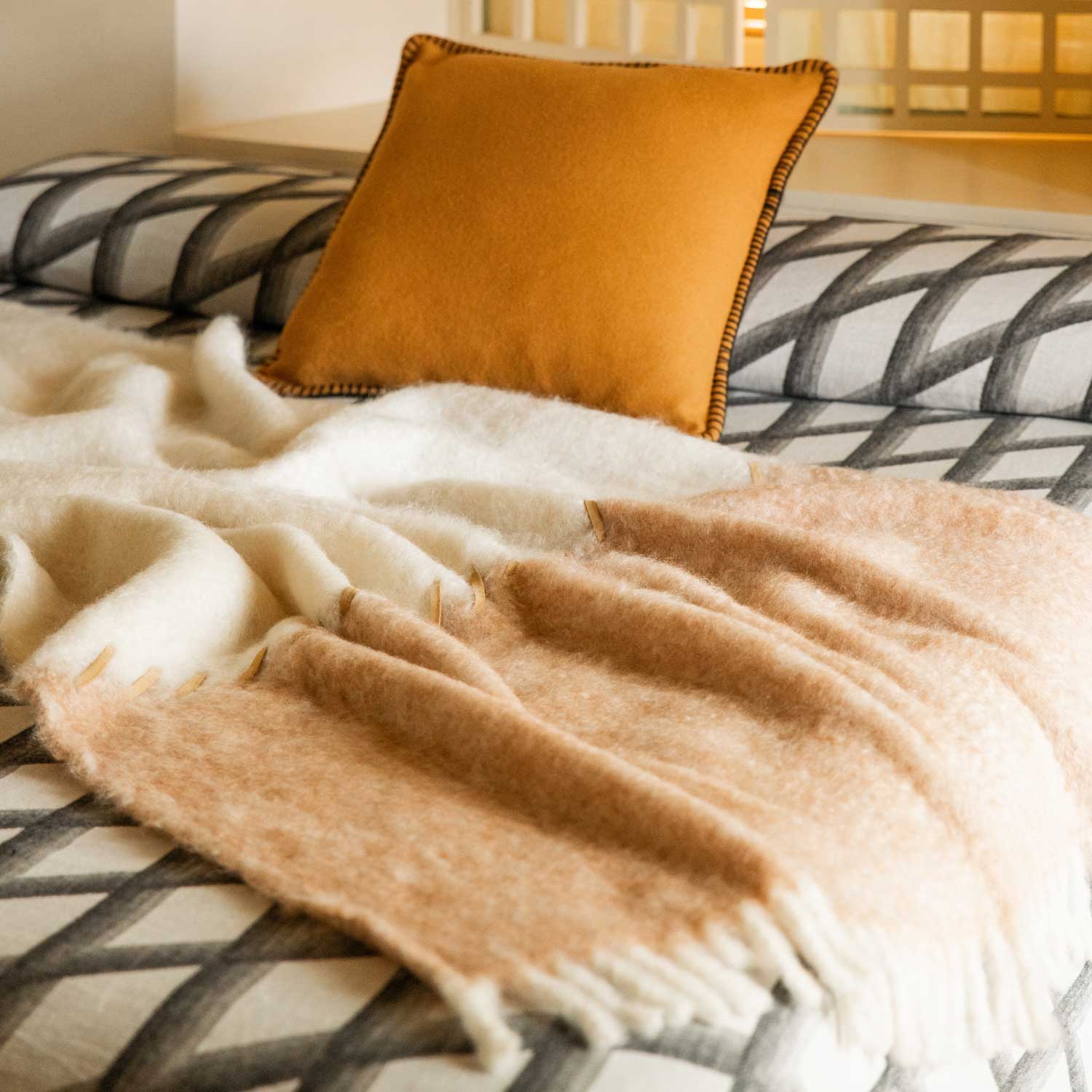A brown merino pillow and a pink and white mohair blanket, separated by brown leather stitching, on a bed.
