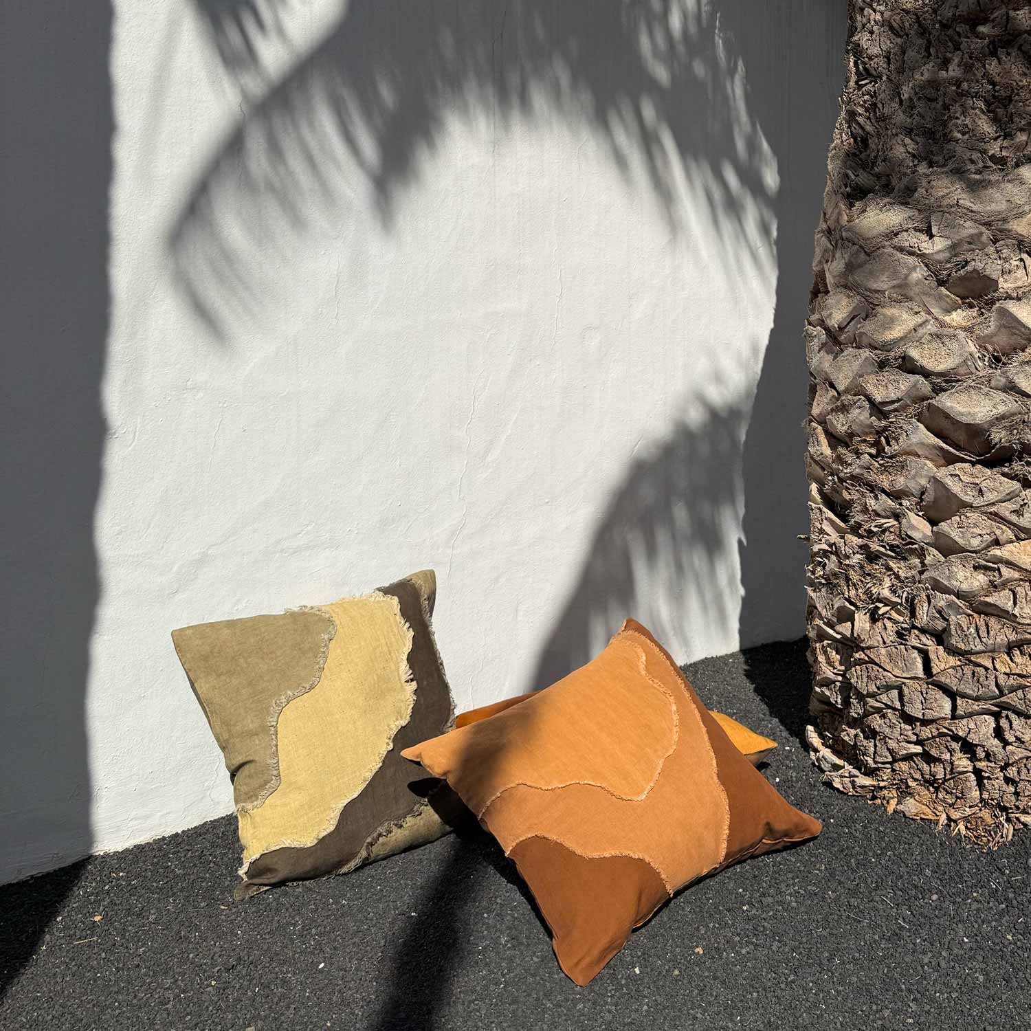 Two patterned pillows on a textured surface with a stone wall in the background