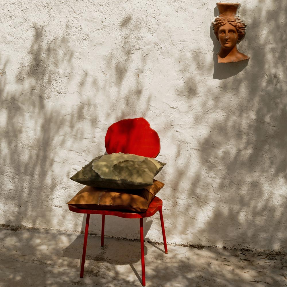 Red chair with linen botanical pillows against a textured white wall