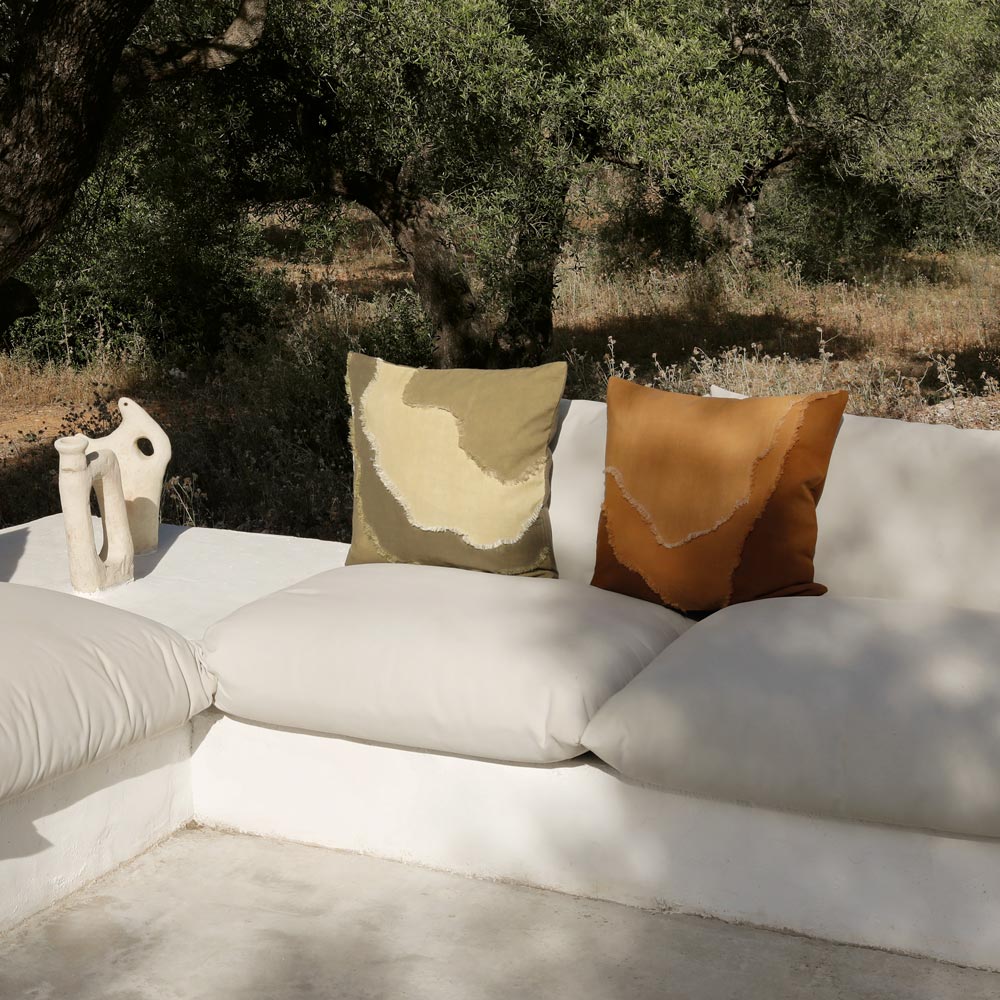White outdoor sofa with patterned pillow against a natural background