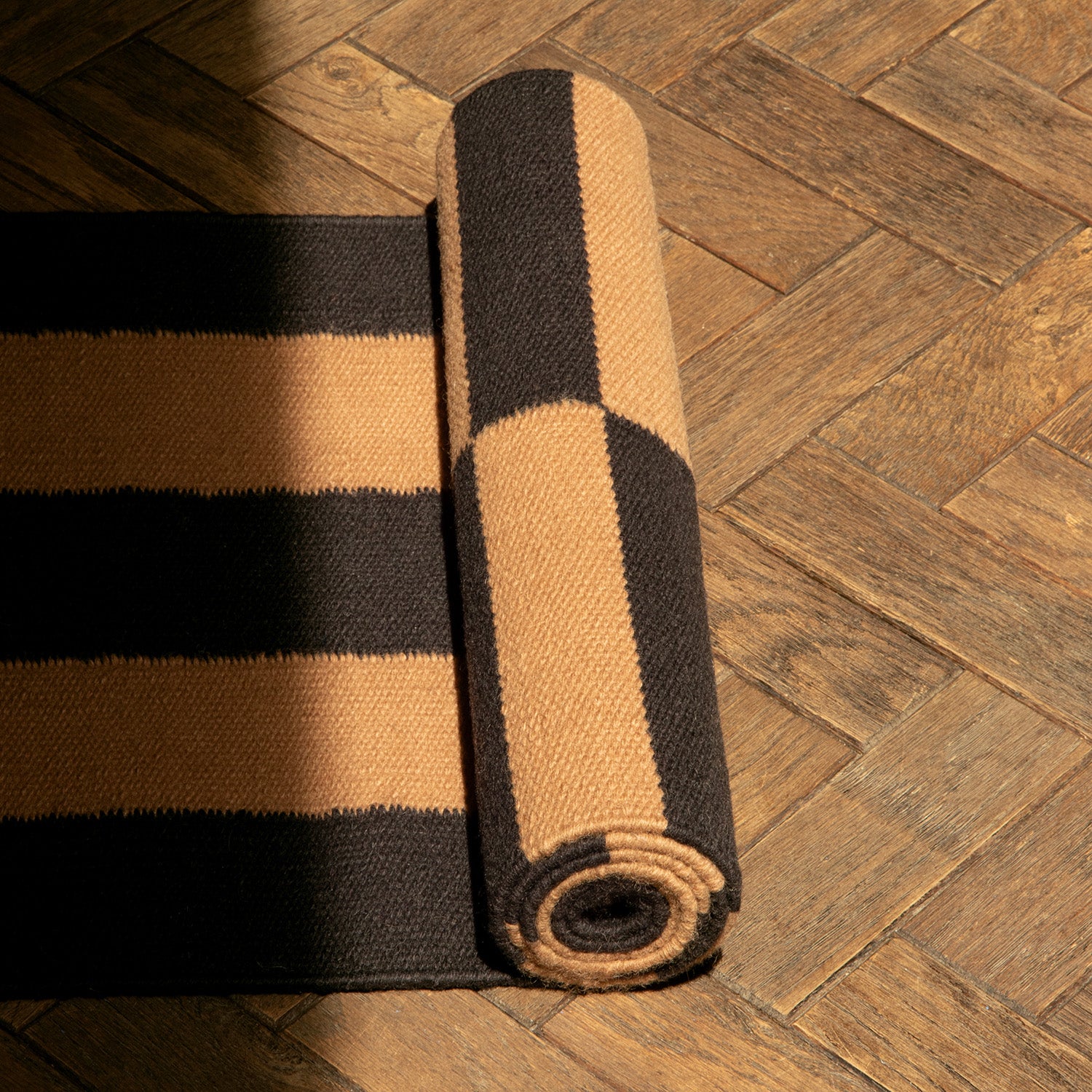 Rolled-up black and beige striped runner rug on a wooden floor