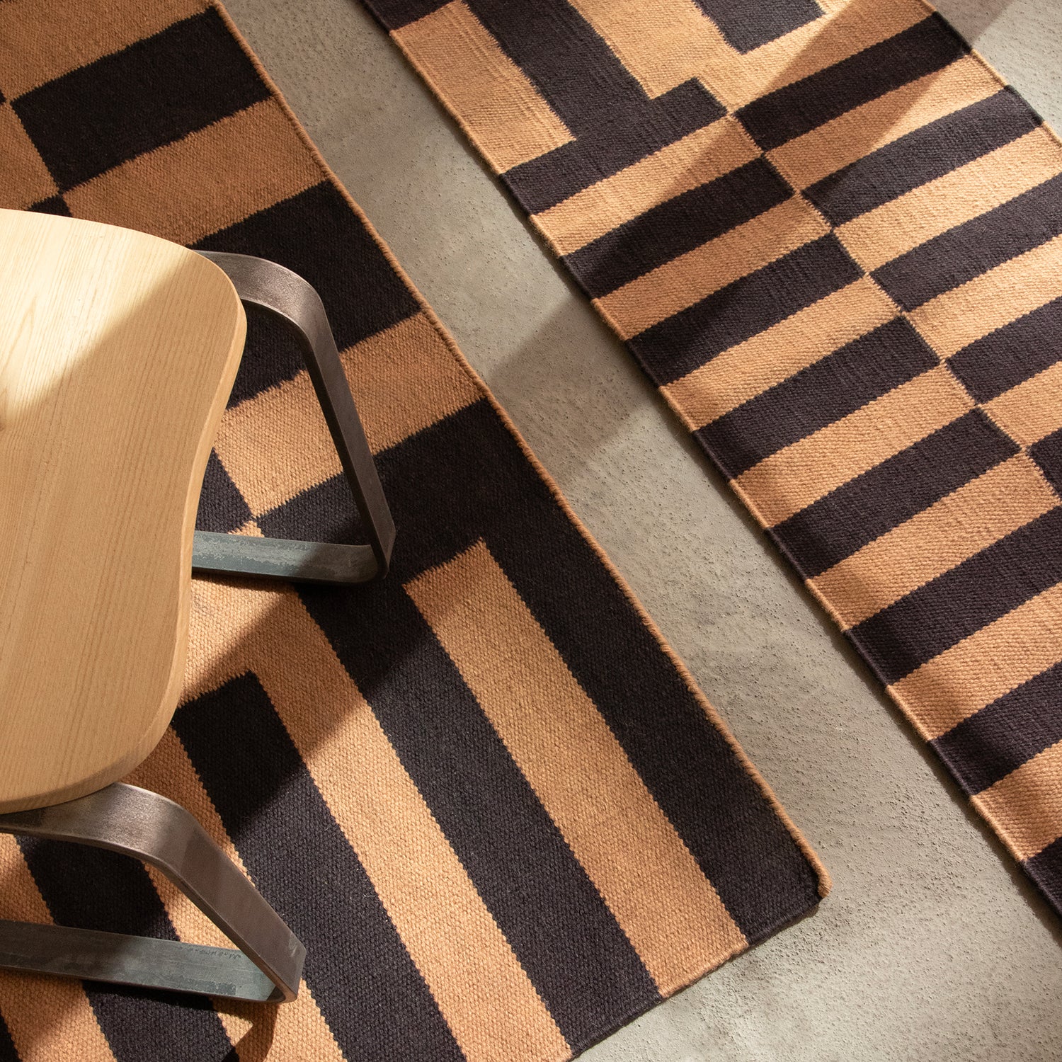 Patterned rug with geometric design on a floor, featuring a chair on it.