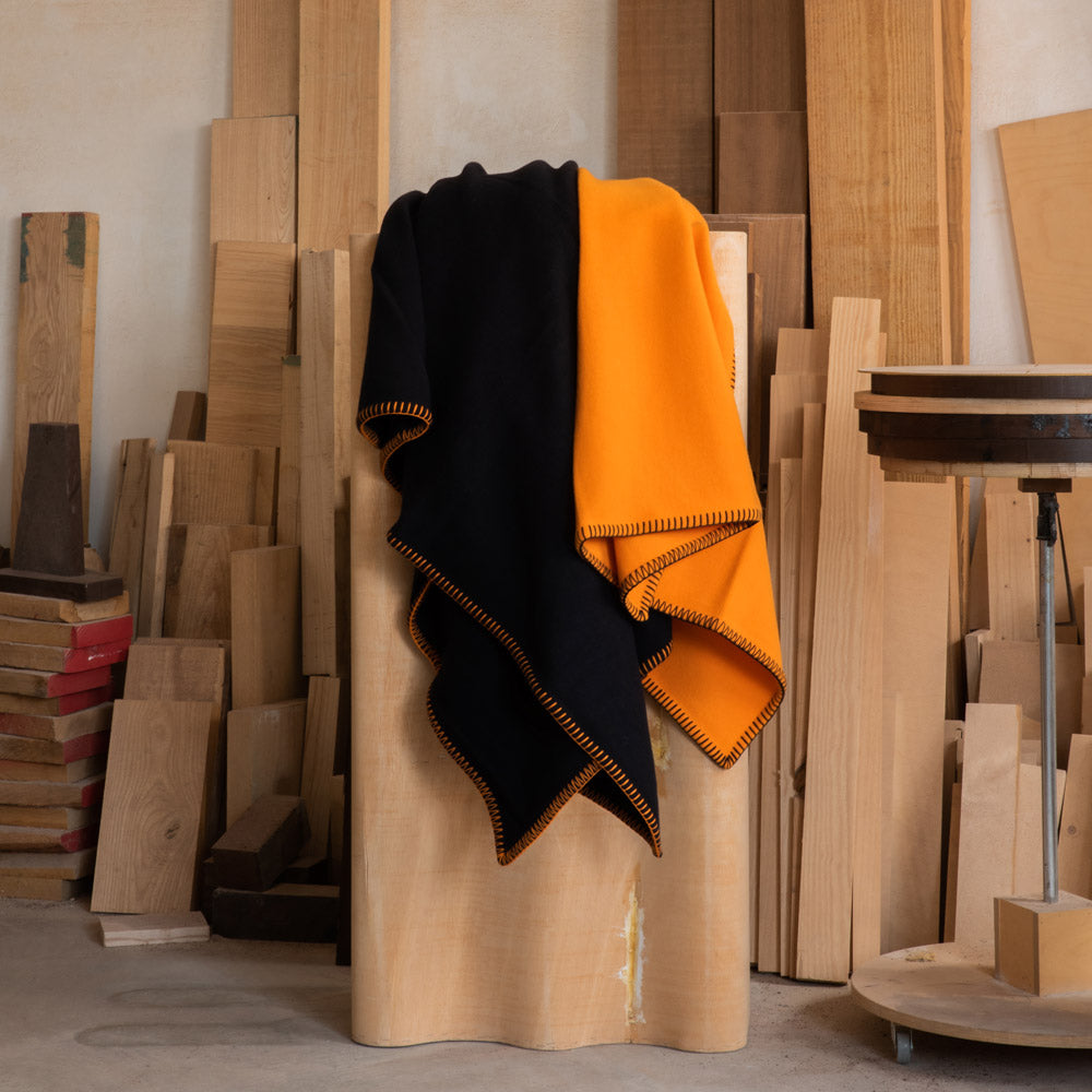 Two merino blankets, one black and one orange, on a display cabinet.
